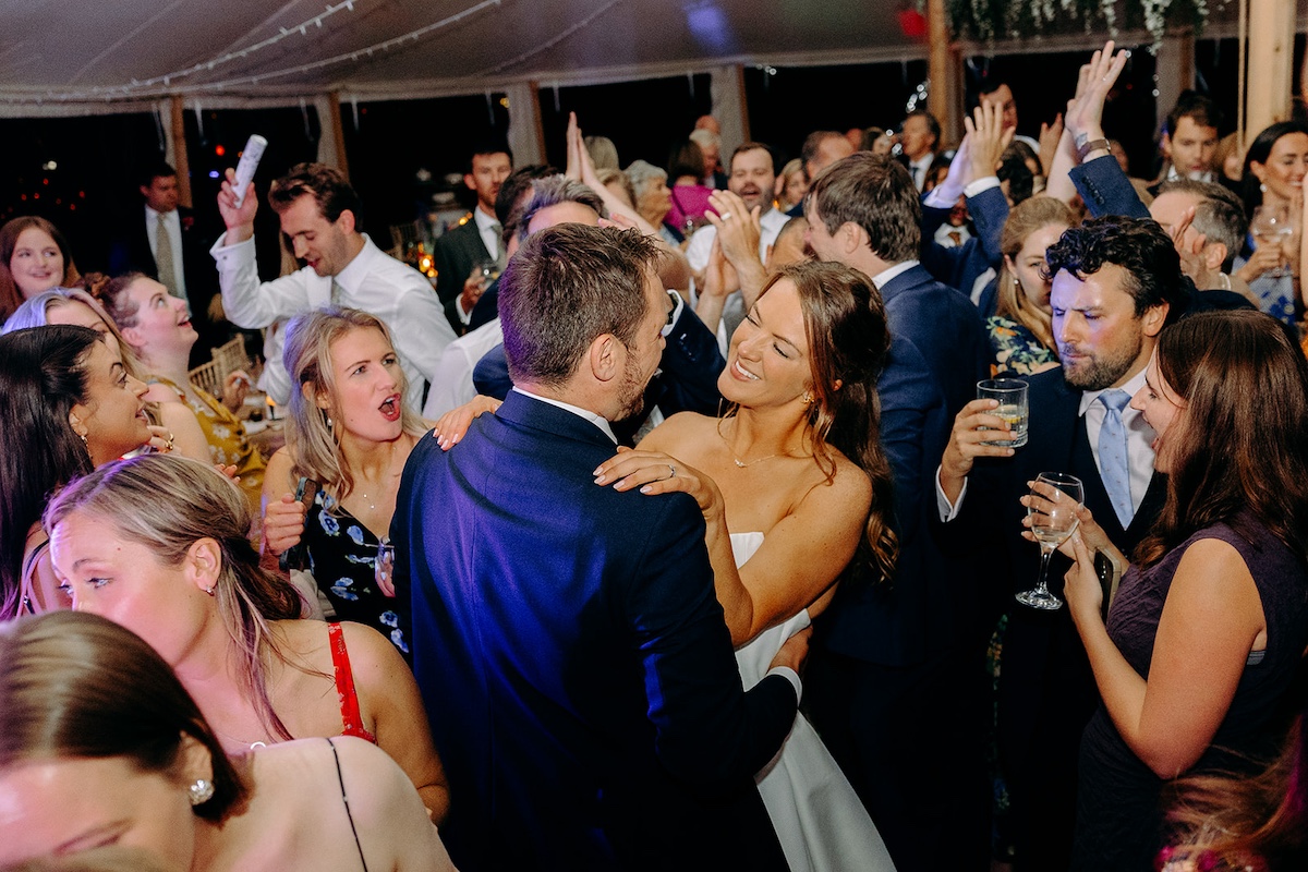 Bride and groom laughing together surrounded by dancing guests at Peak District marquee wedding.