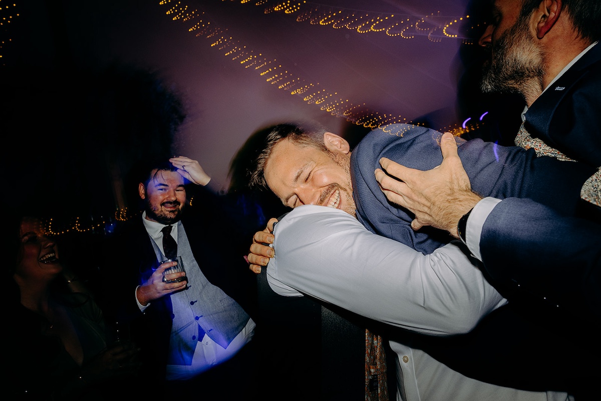Groom singing along on dance floor with friends during late-night Eyam Hall wedding party.