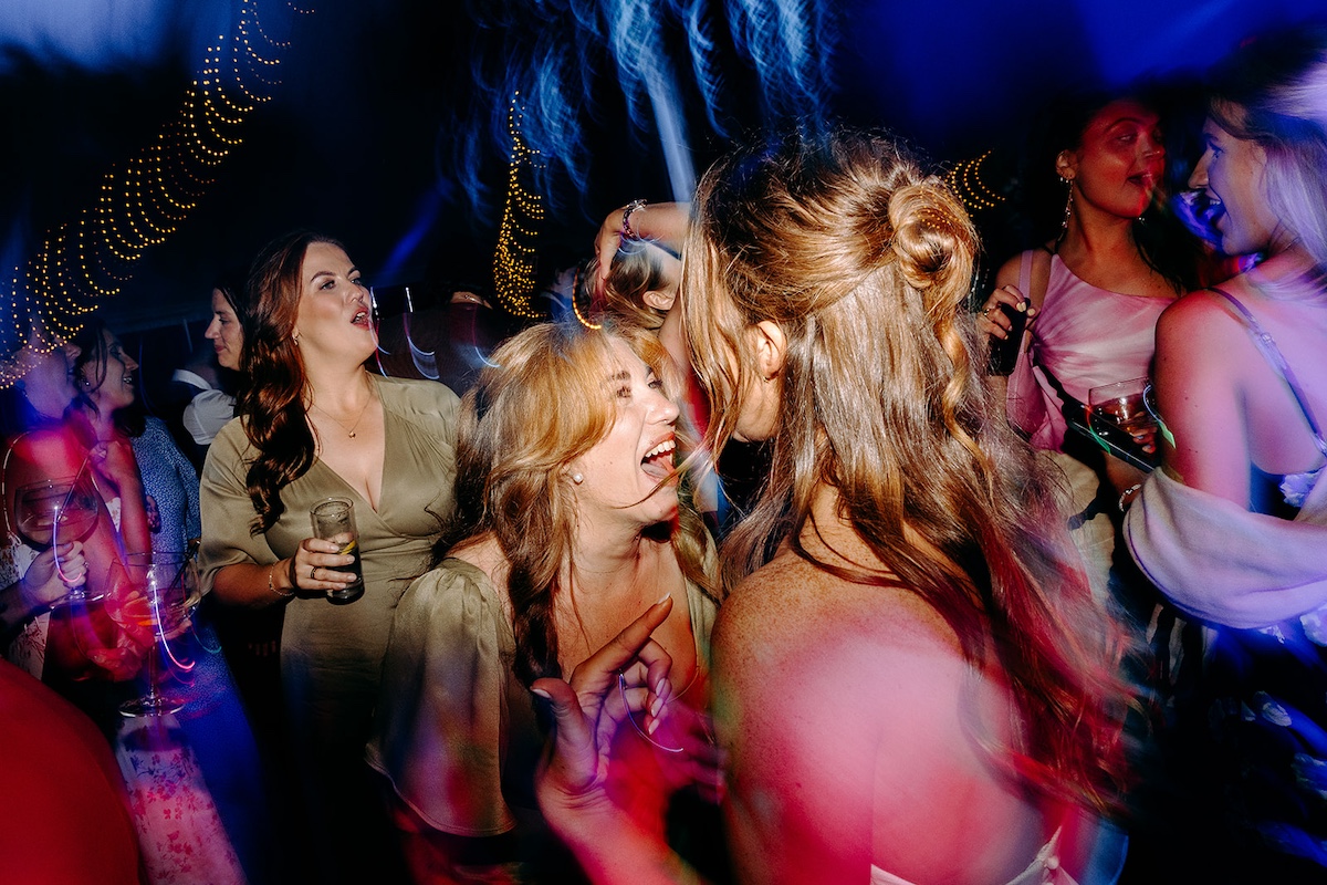 Guests embracing and laughing on busy dance floor during Peak District wedding reception.