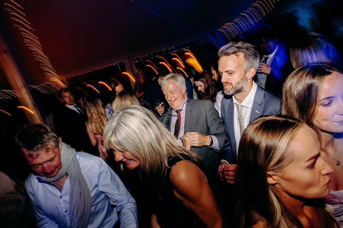Guests embracing and laughing on busy dance floor during Peak District wedding reception.