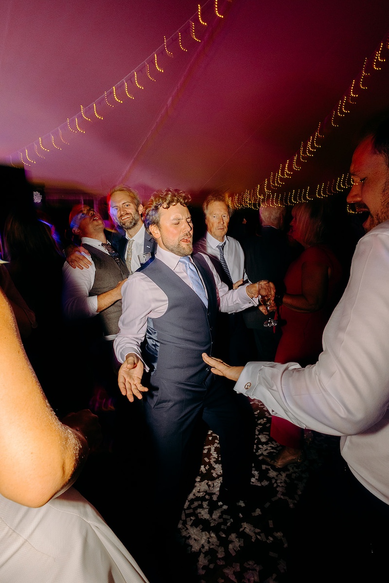 Energetic dance floor moment with guests cheering and confetti still on ground at Eyam Hall wedding.