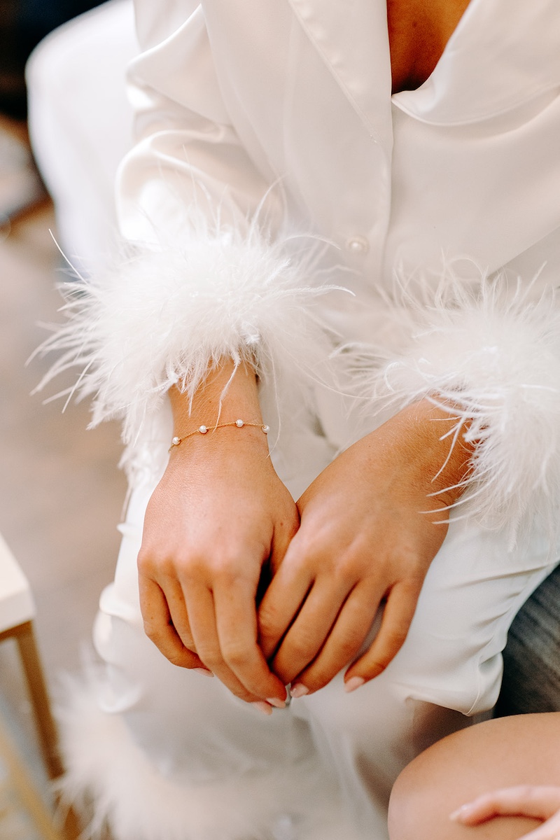 Close-up of bride’s hands resting on her lap with feather cuffs visible during prep at Eyam Hall.