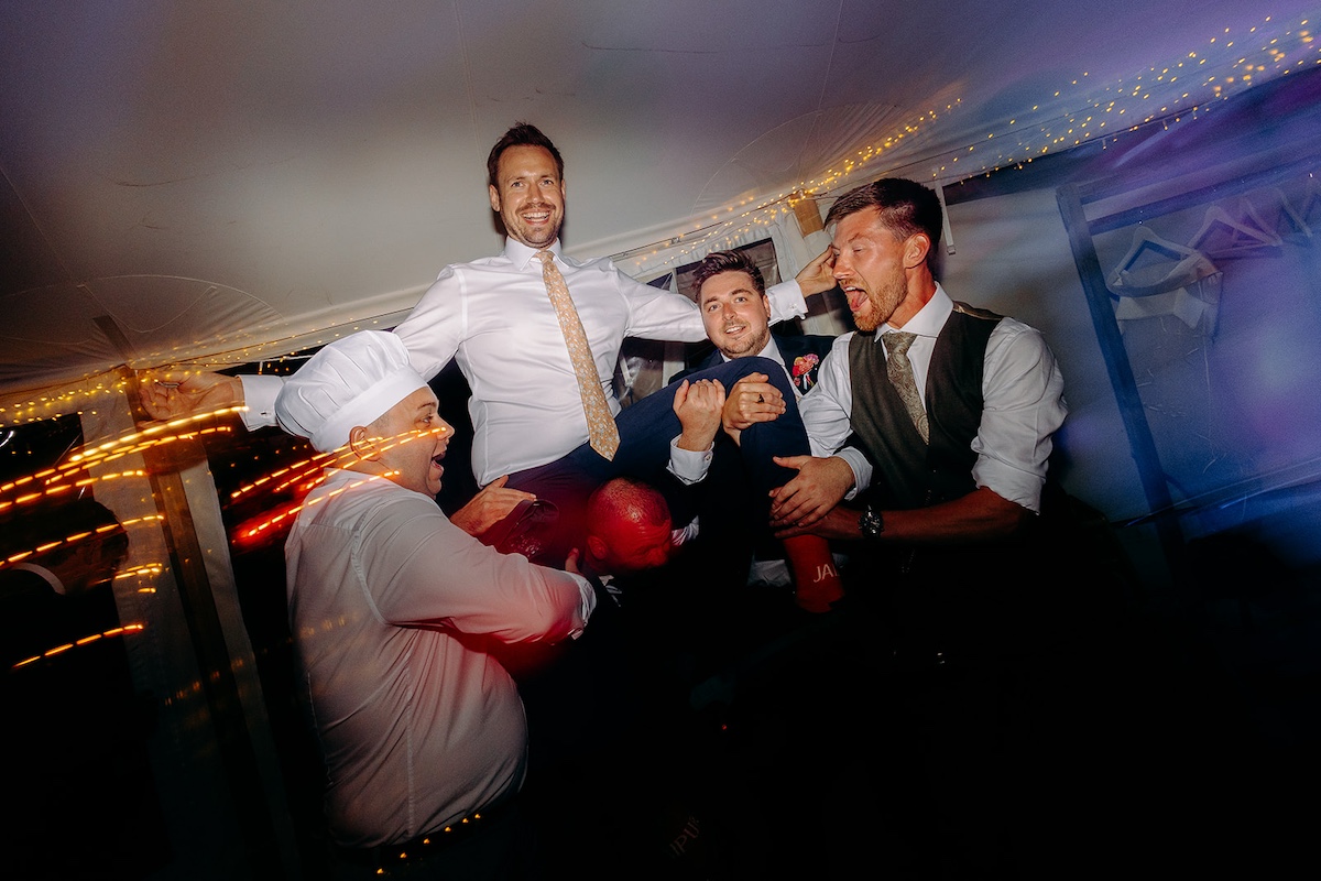 Groom being lifted by groomsmen while laughing on the dance floor – fun wedding photography in Derbyshire.