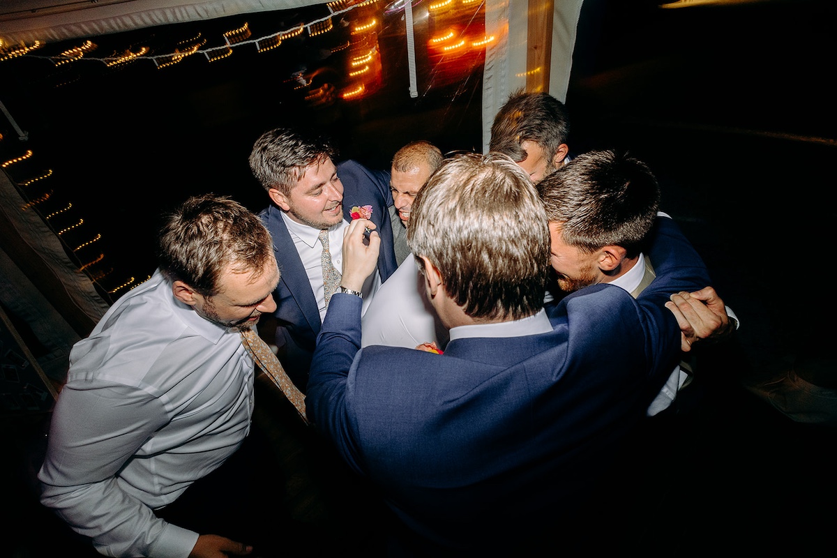 Groomsmen hugging on dance floor at end of the night, surrounded by guests – emotional finish to Peak District wedding day.