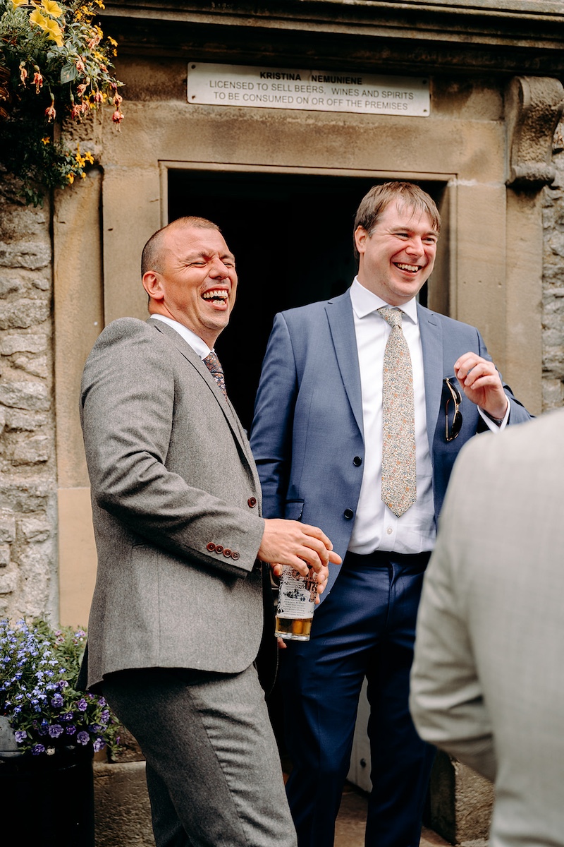 Groom and groomsmen chatting in the street with stone cottages behind them in Eyam village.