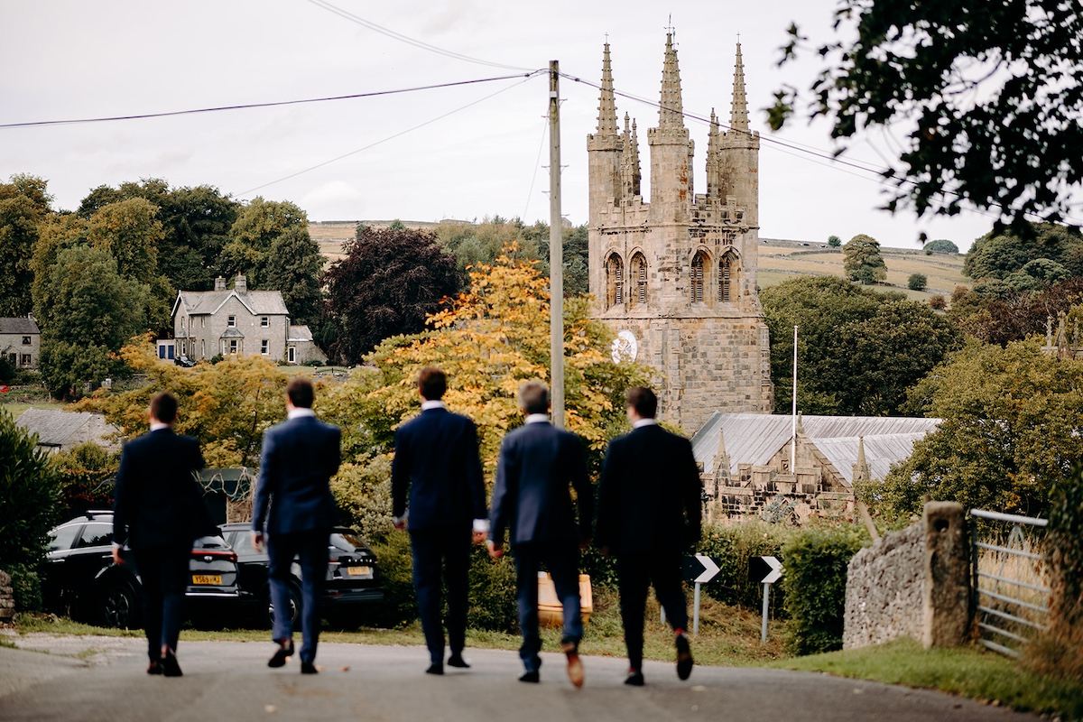 Wide shot of Eyam village street with guests arriving for wedding ceremony in the Peak District.