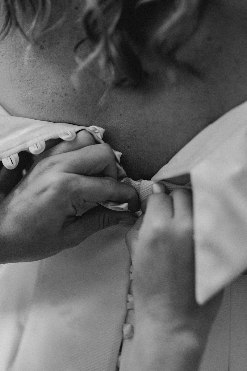 Detailed shot of bridesmaids buttoning up wedding dress during bridal prep – Eyam Hall wedding photography.