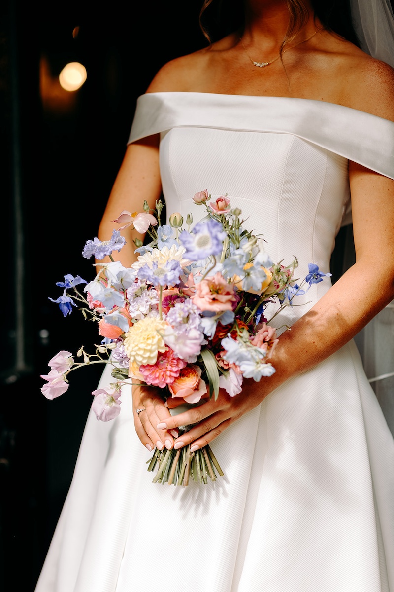 Bride standing in doorway holding bouquet, soft natural light portrait before ceremony at Eyam Hall.