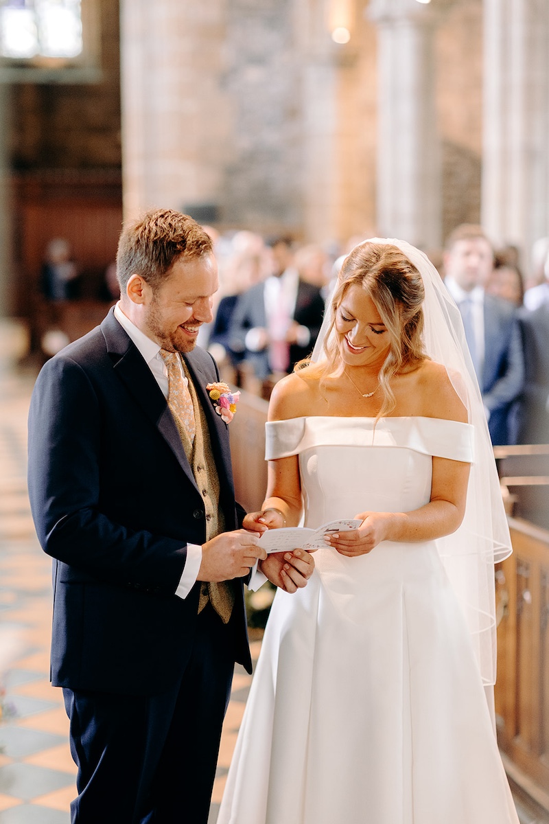 Groom reading vows from paper while bride listens beside him at Eyam Hall wedding ceremony.