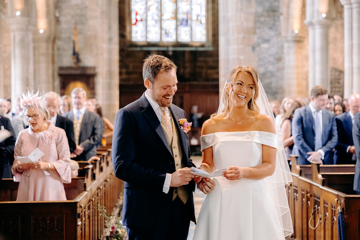 Bride and groom laughing together during vows inside Eyam church – natural Peak District wedding photography.
