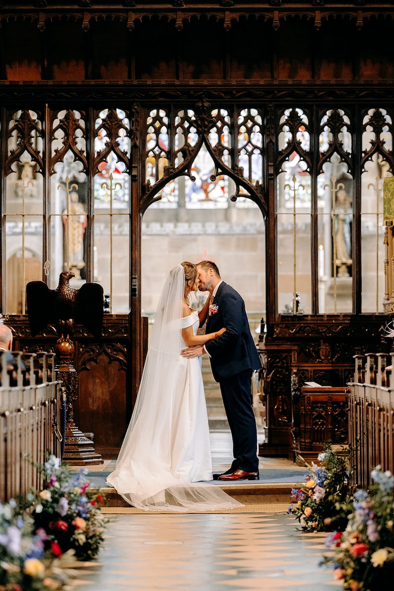 Bride and groom sharing a kiss at the altar inside Eyam church during wedding ceremony.