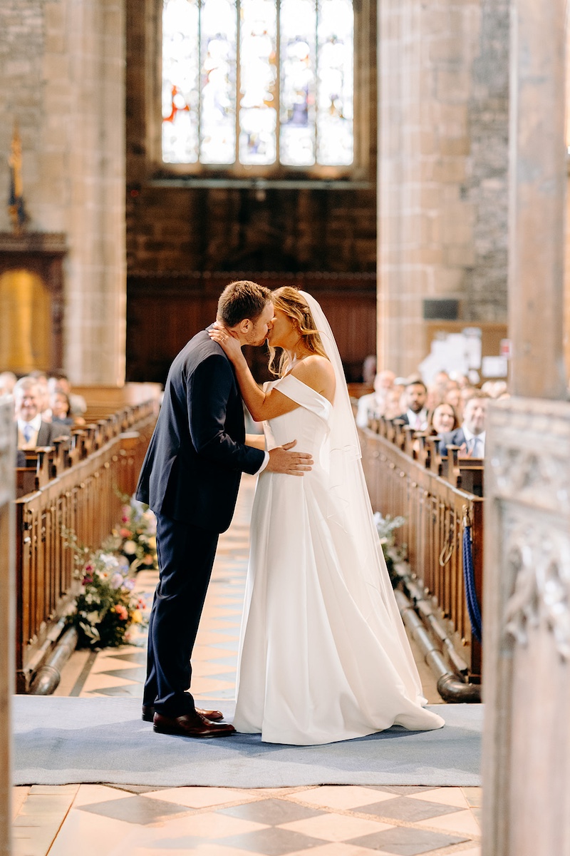 Bride and groom sharing a kiss at the altar inside Eyam church during wedding ceremony.