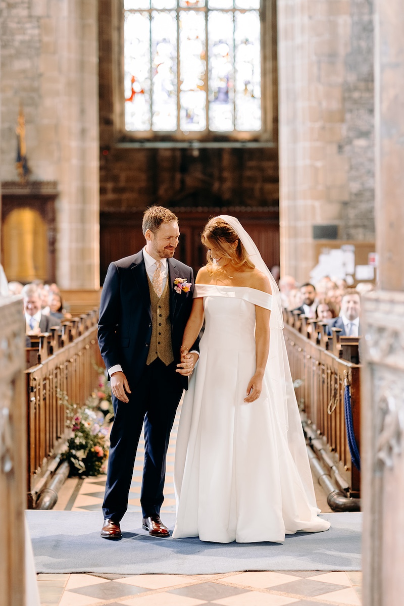 Bride and groom standing together smiling after ceremony inside Eyam church.