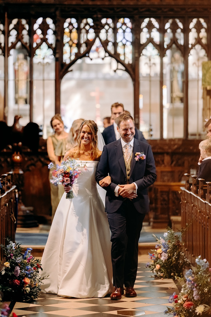 Bride and groom walking back down the aisle together after ceremony at Eyam Hall church.