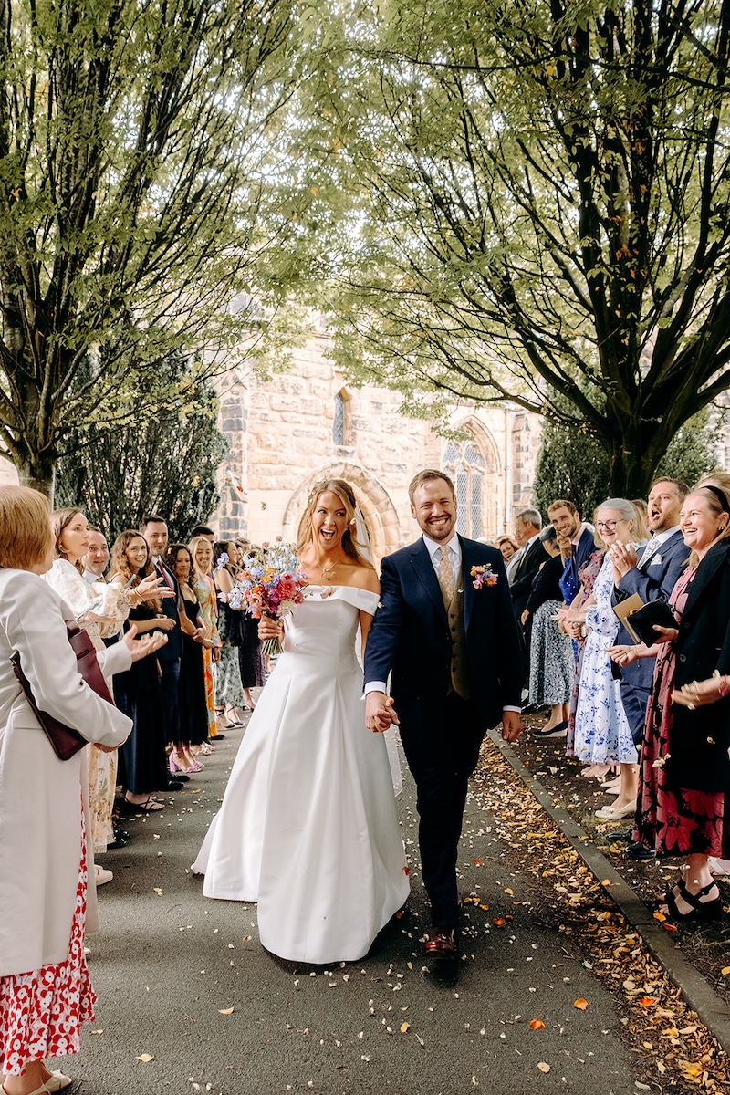 Confetti being thrown over bride and groom as they walk through guests at Eyam Hall wedding.
