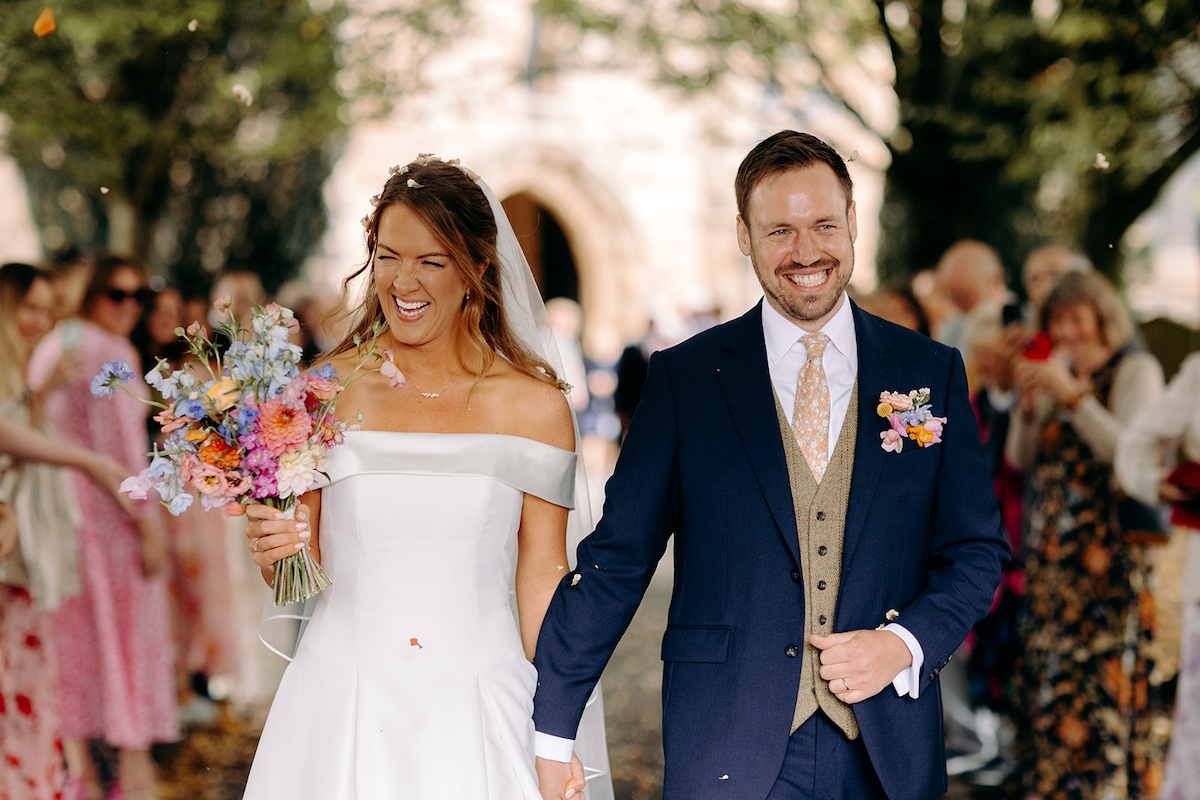 Couple laughing together surrounded by friends and family during confetti throw in Eyam village.