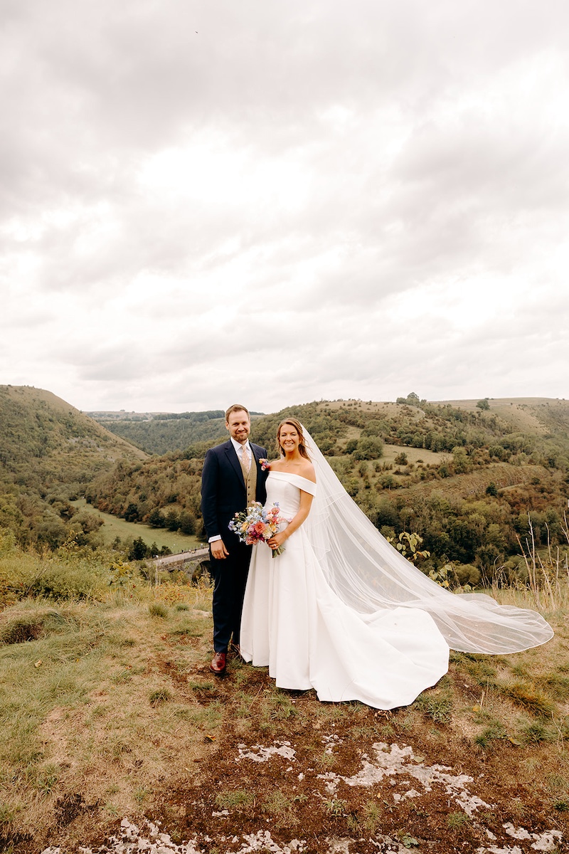 Bride and groom on moorland with dramatic Peak District hills behind – natural Derbyshire wedding photography.
