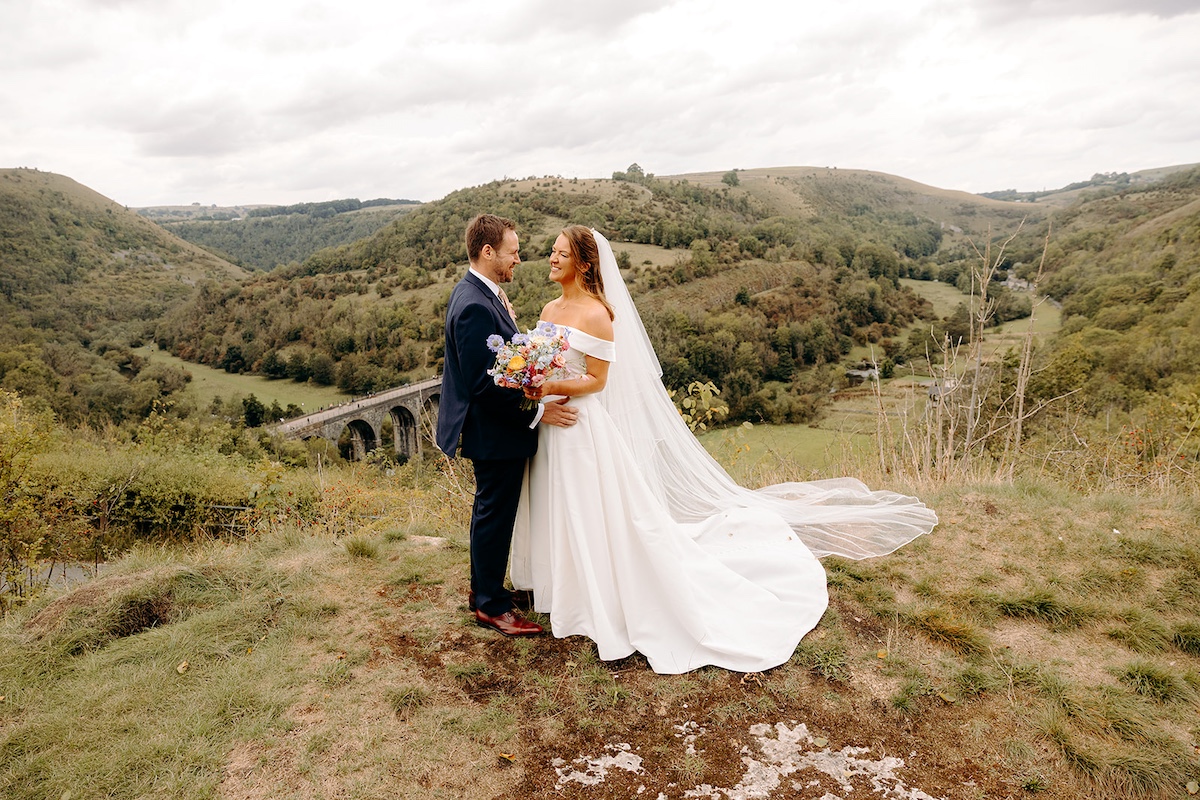 Bride and groom walking through moorland, laughing together after Eyam Hall wedding ceremony.