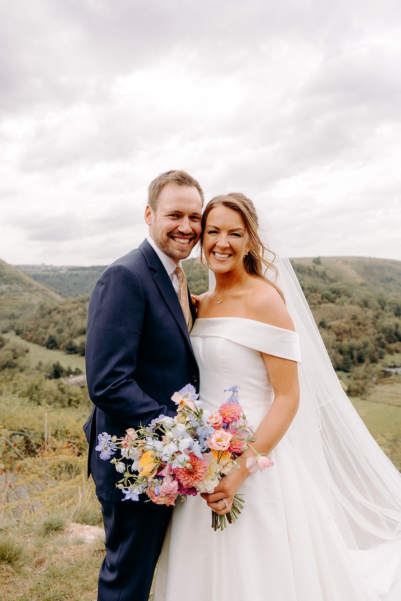 Couple holding hands and walking toward camera through heather in Peak District – relaxed wedding photography.