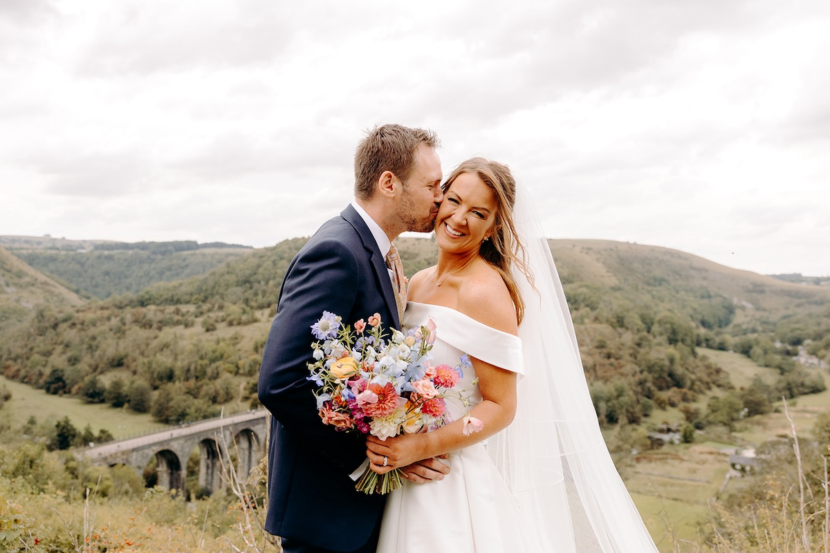 Close-up of bride and groom embracing in wild Peak District landscape after Eyam Hall wedding.