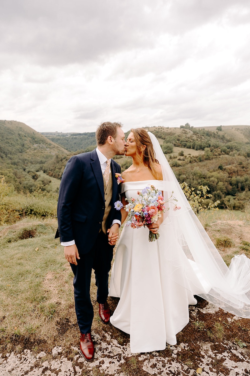 Couple holding hands and walking toward camera through heather in Peak District – relaxed wedding photography.