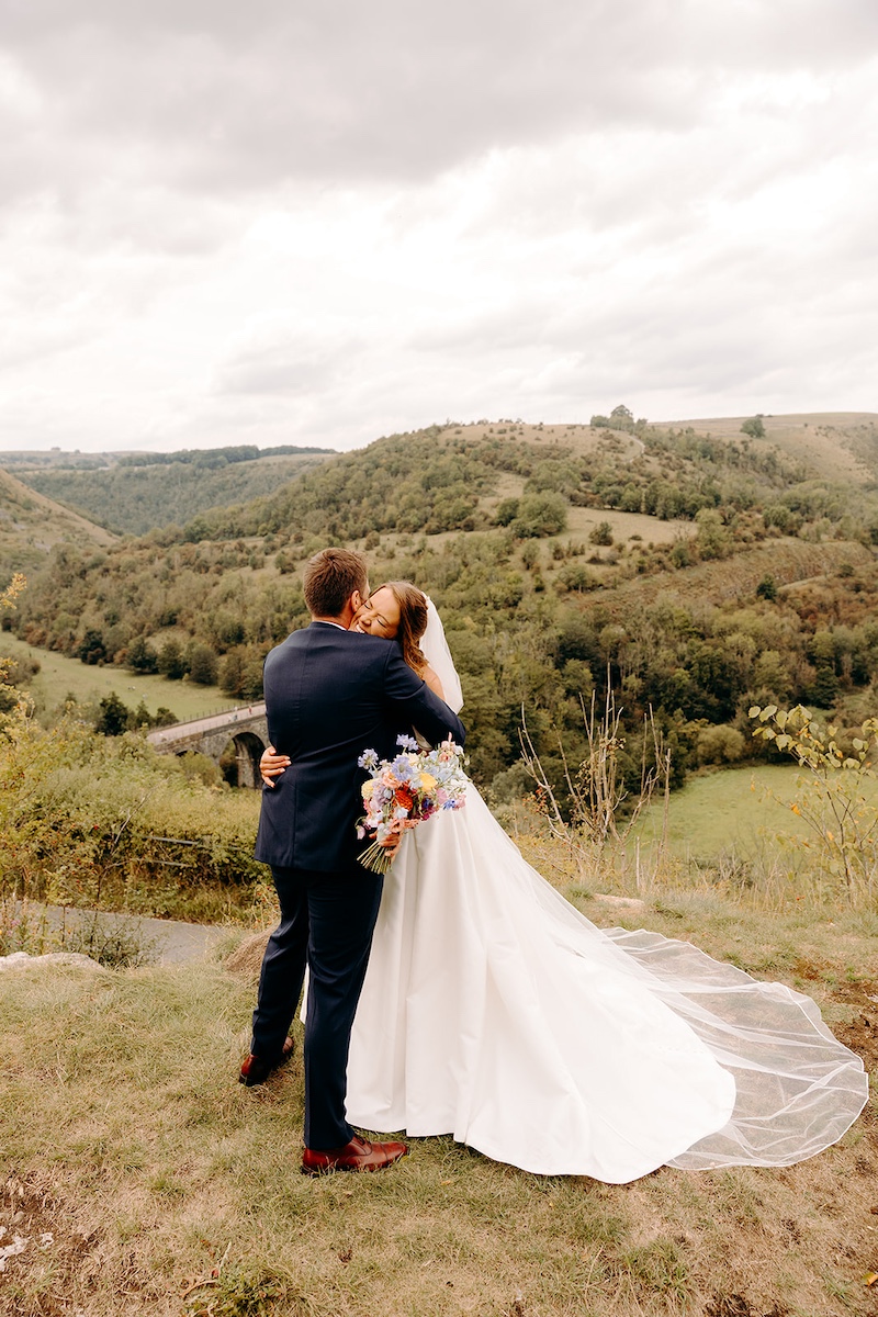 Bride and groom embracing in wild Peak District landscape after Eyam Hall wedding.