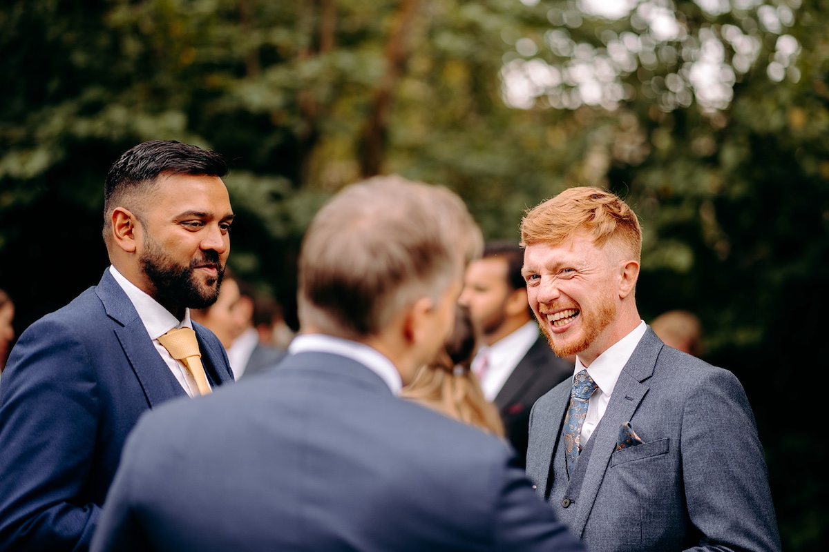 Wedding guests chatting and laughing outside marquee during Eyam Hall reception drinks.