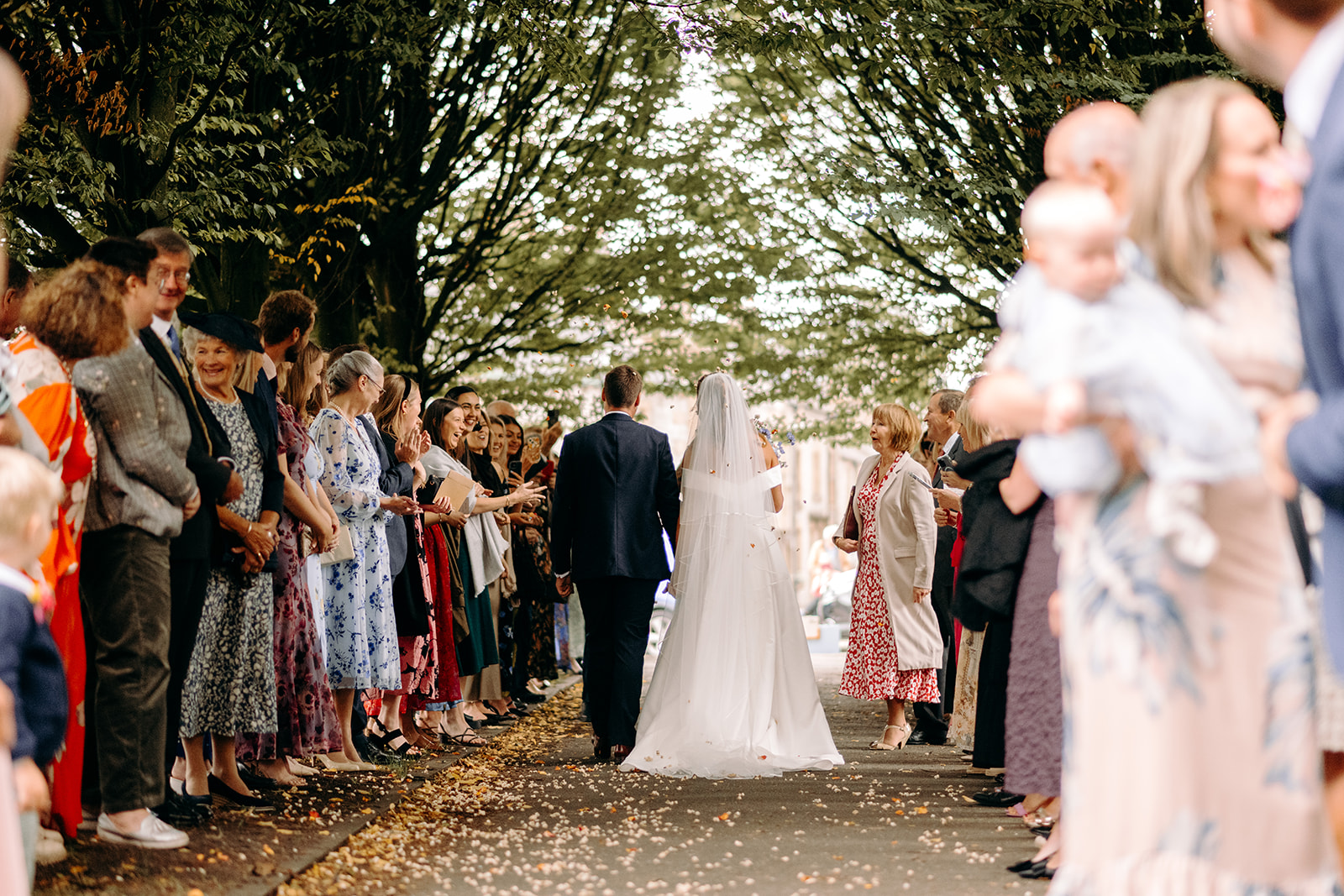 Couple laughing together surrounded by friends and family during confetti throw in Eyam village.