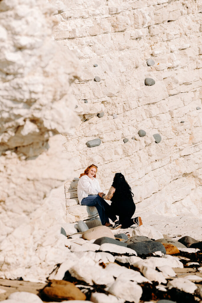 Secret beach proposal at Flamborough Head in North Yorkshire with couple sitting together on white chalk rocks overlooking the sea