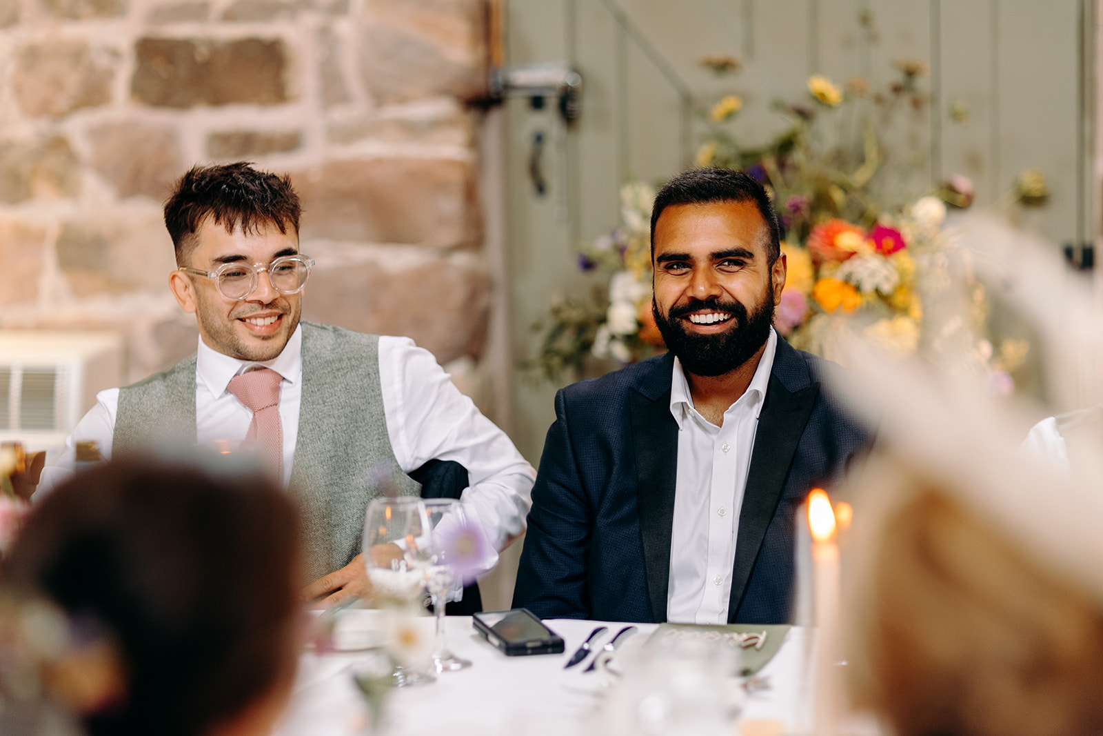 Two guests smiling together during speeches at an Ashes Barns wedding.