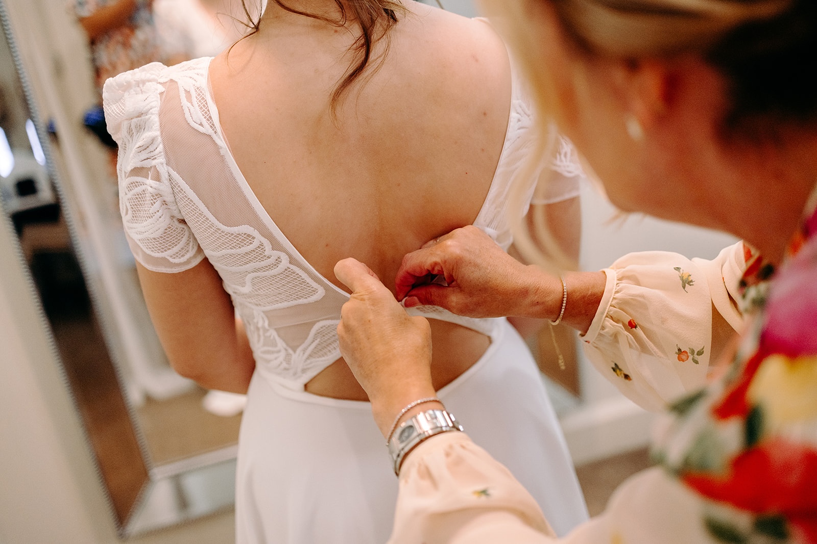 Close-up of mother of the bride fastening dress buttons during wedding morning prep.