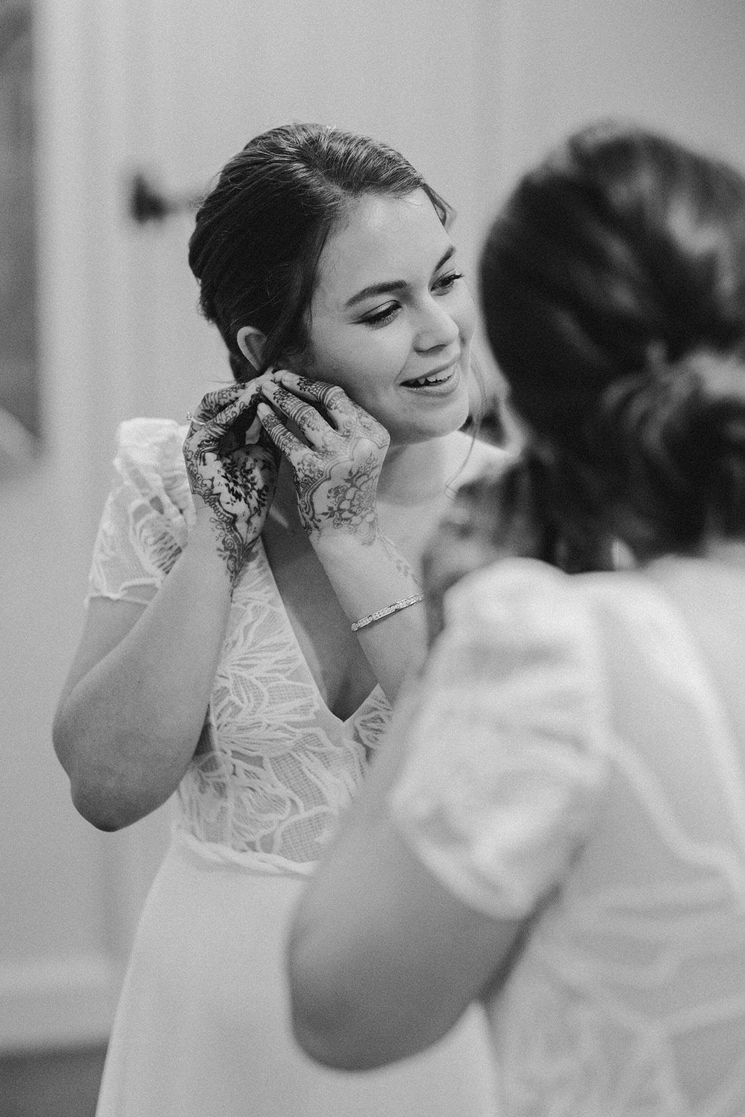 Black and white moment of the bride smiling during final wedding preparations at Ashes Barns, with detail henna on her hands.