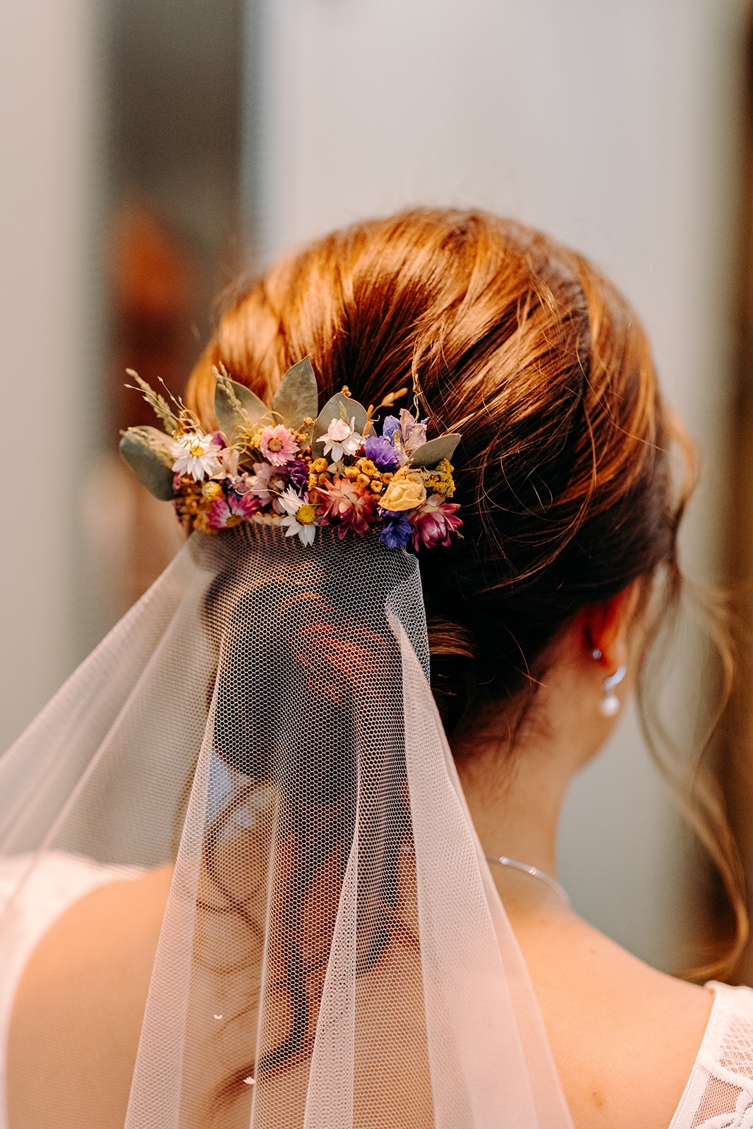 Close-up of one bride’s low bun hairstyle finished with colourful, dried wedding flowers.