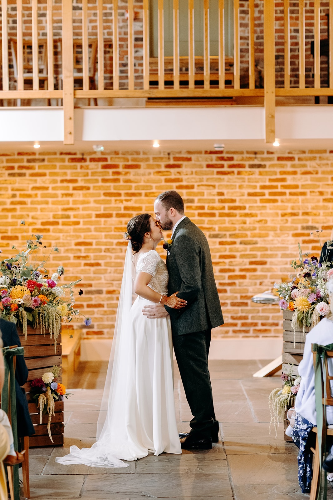 Wide shot of the couple kissing beneath wooden beams during their Ashes Barns wedding ceremony.