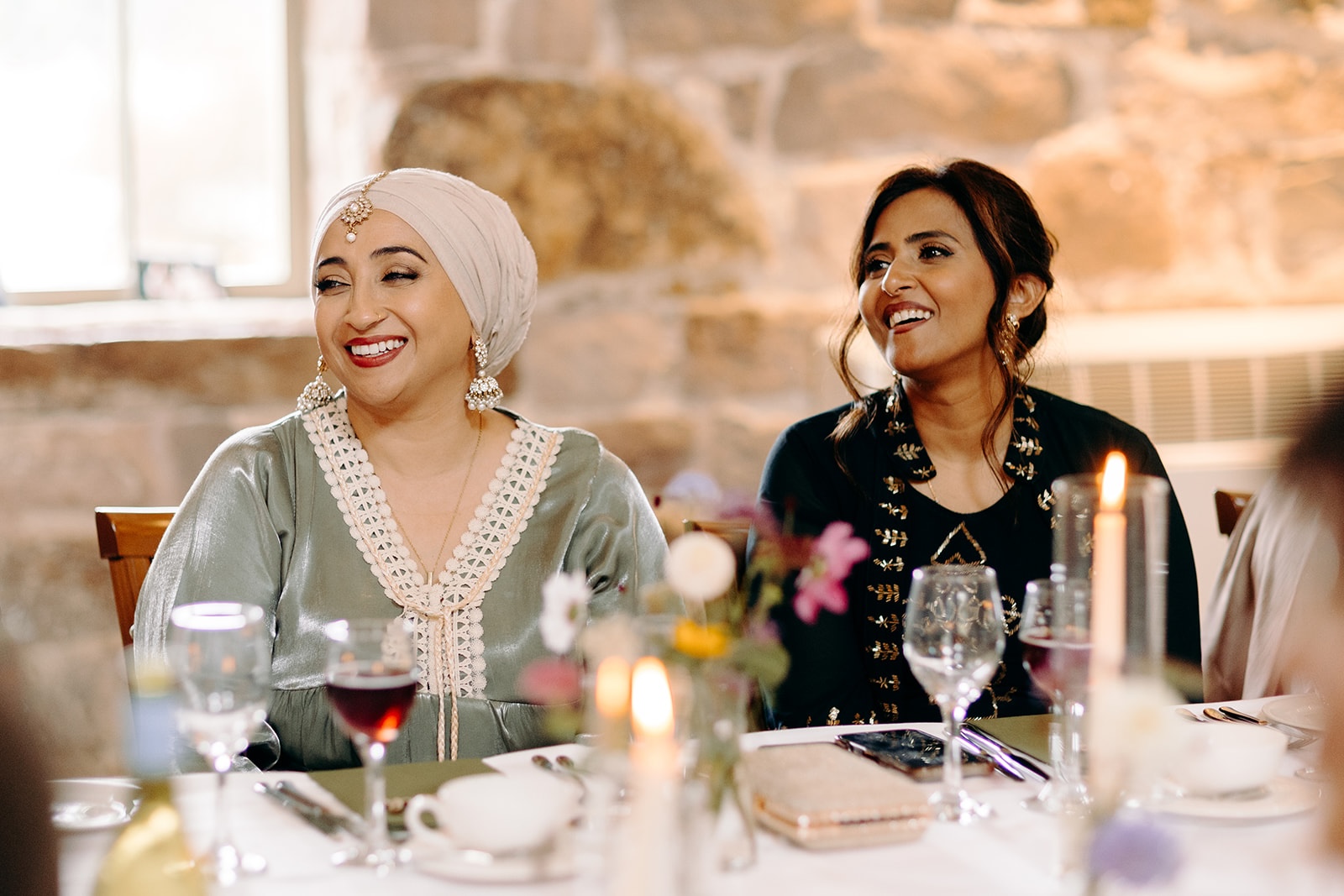 Two guests smiling together during speeches at an Ashes Barns wedding.
