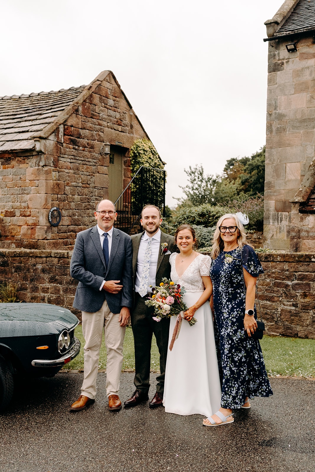 Group photo of the wedding party outside Ashes Barns with stone buildings behind them.