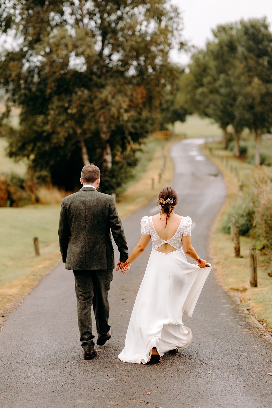 Newlyweds walking hand in hand down a country lane near Ashes Barns.