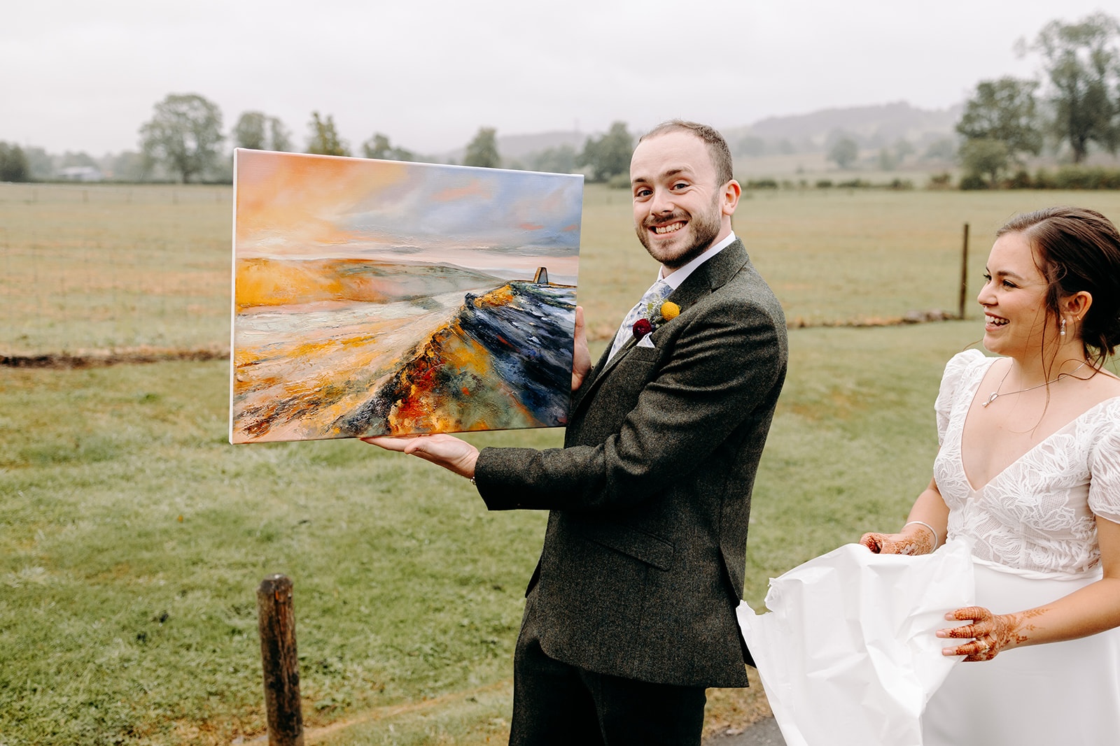 One partner holding up a colourful painting during playful wedding portraits near Ashes Barns.