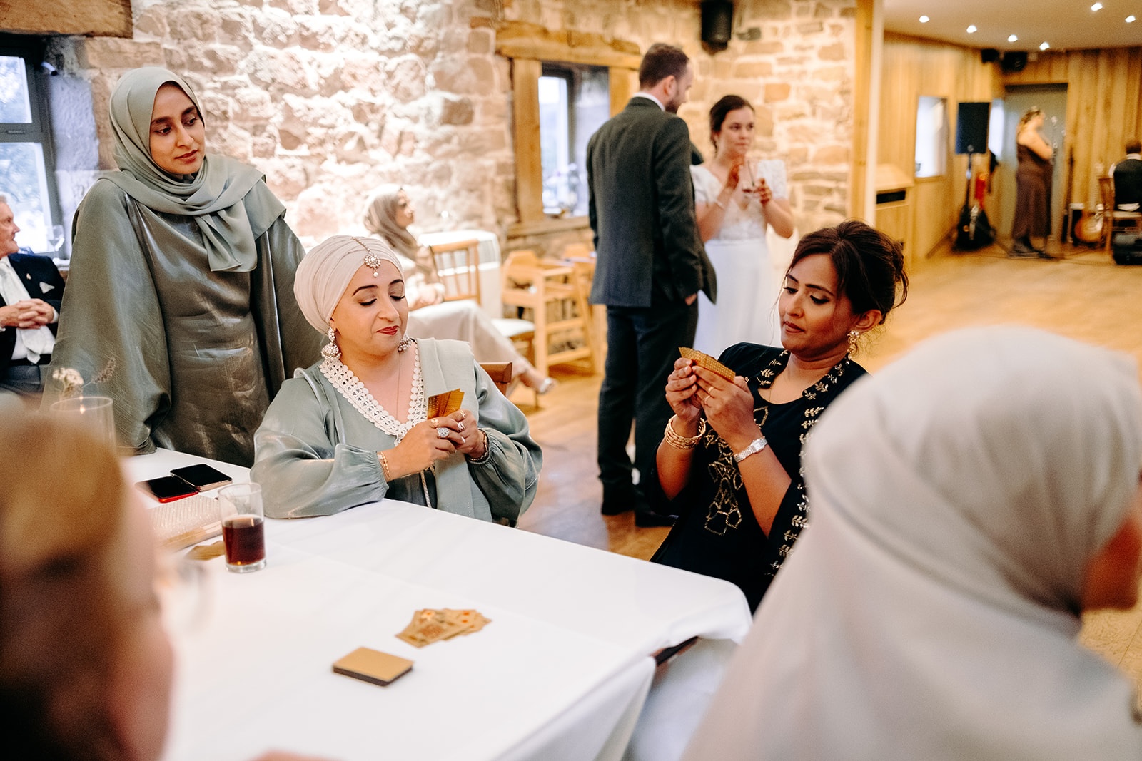 Guests laughing together over card games and drinks during the Ashes Barns wedding evening.