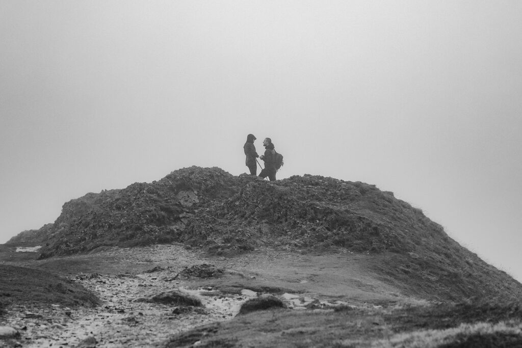 Silhouetted couple standing on misty Lake District fell after secret mountain proposal at sunrise