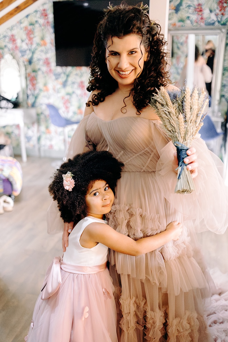 Bride hugging a young flower girl while getting ready at The Wellbeing Farm, a sweet preparation moment captured with natural documentary wedding photography.