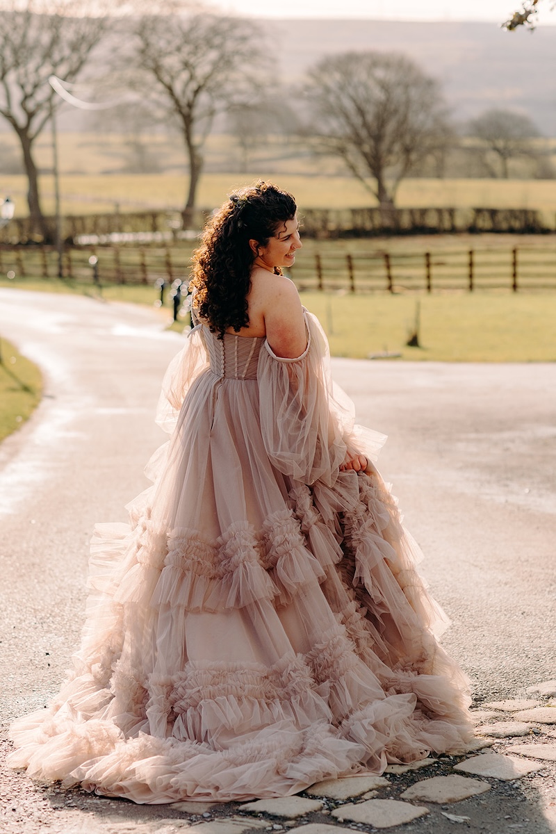 Bride walking through the courtyard in her layered, All Who Wander wedding dress during her February wedding day.