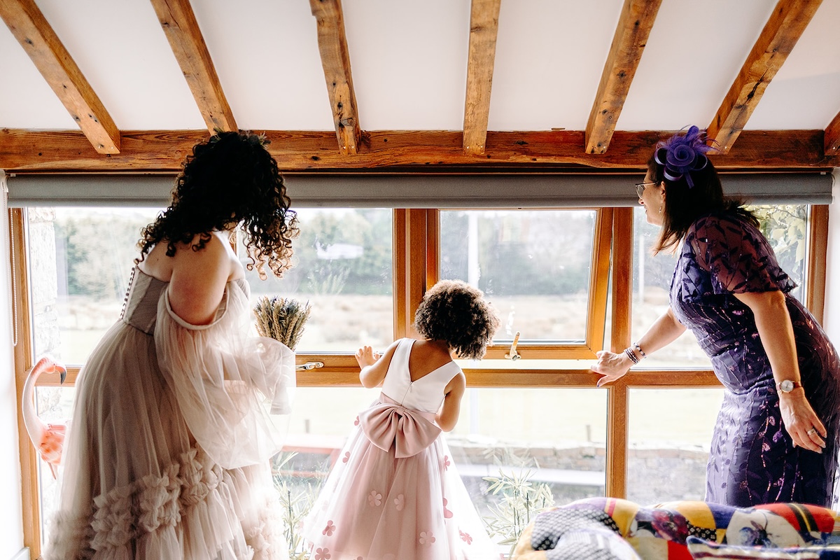 Bride and flower girl looking out of the window together during morning preparations for a February wedding at The Wellbeing Farm, photographed with relaxed wedding photography.