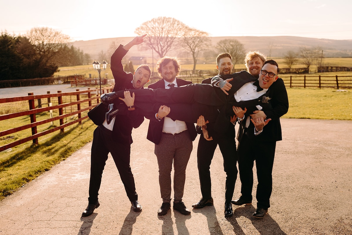 Groomsmen lifting a friend into the air during fun wedding party portraits, captured with relaxed documentary wedding photography.