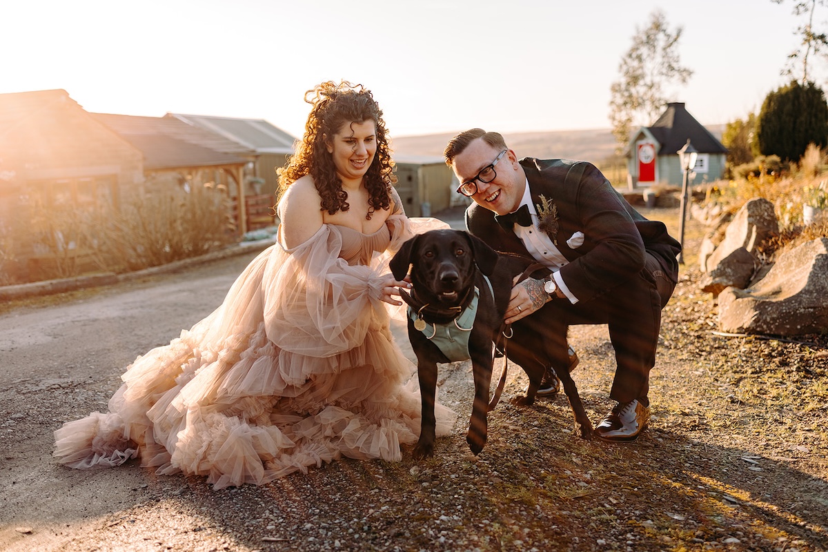 Couple cuddling their dog while sitting outside the venue courtyard at The Wellbeing Farm winter wedding.