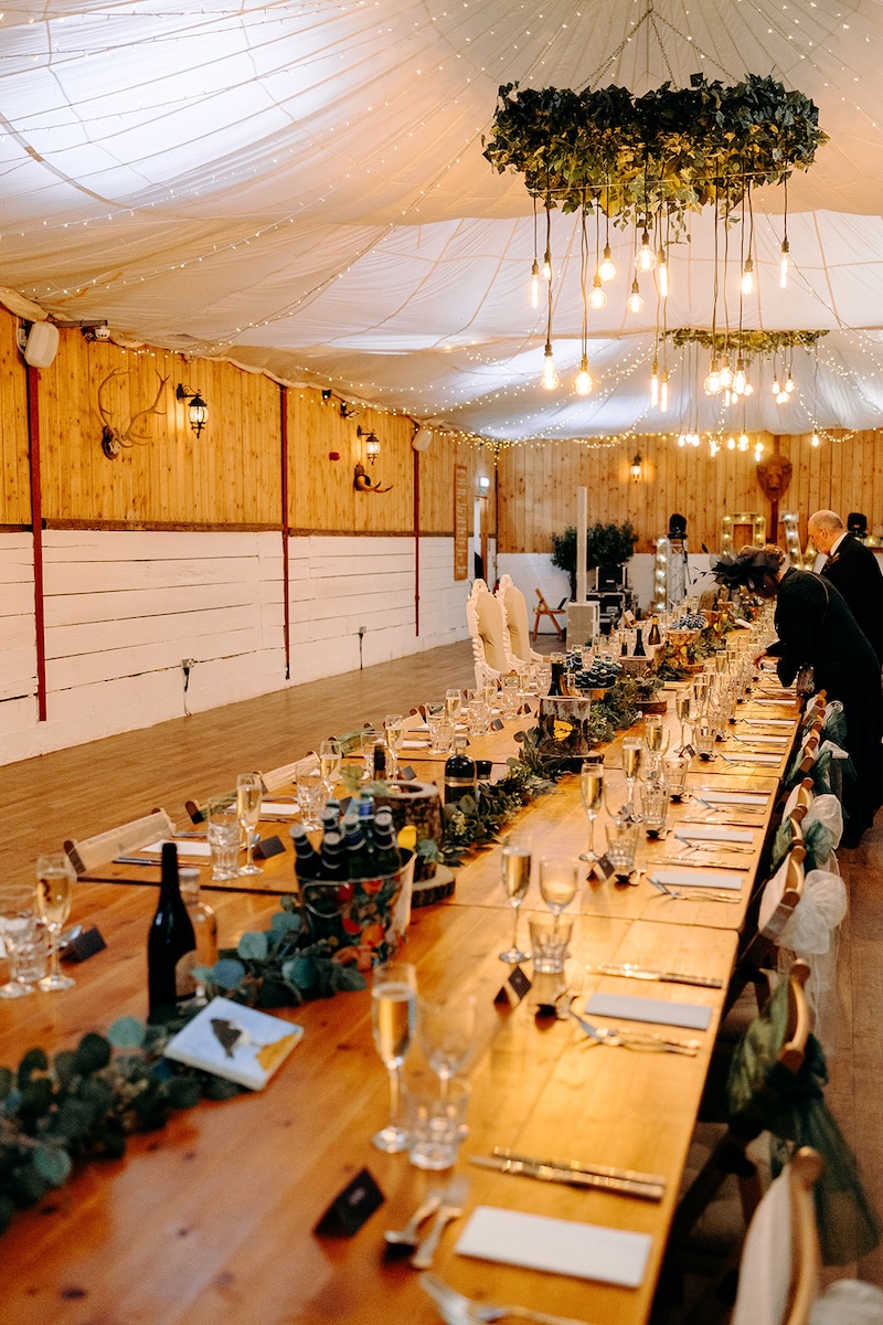 Long banquet tables prepared for the wedding breakfast inside the barn reception space at The Wellbeing Farm.
