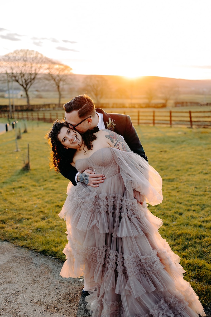Couple cuddling together in the fields during relaxed golden hour wedding photography.