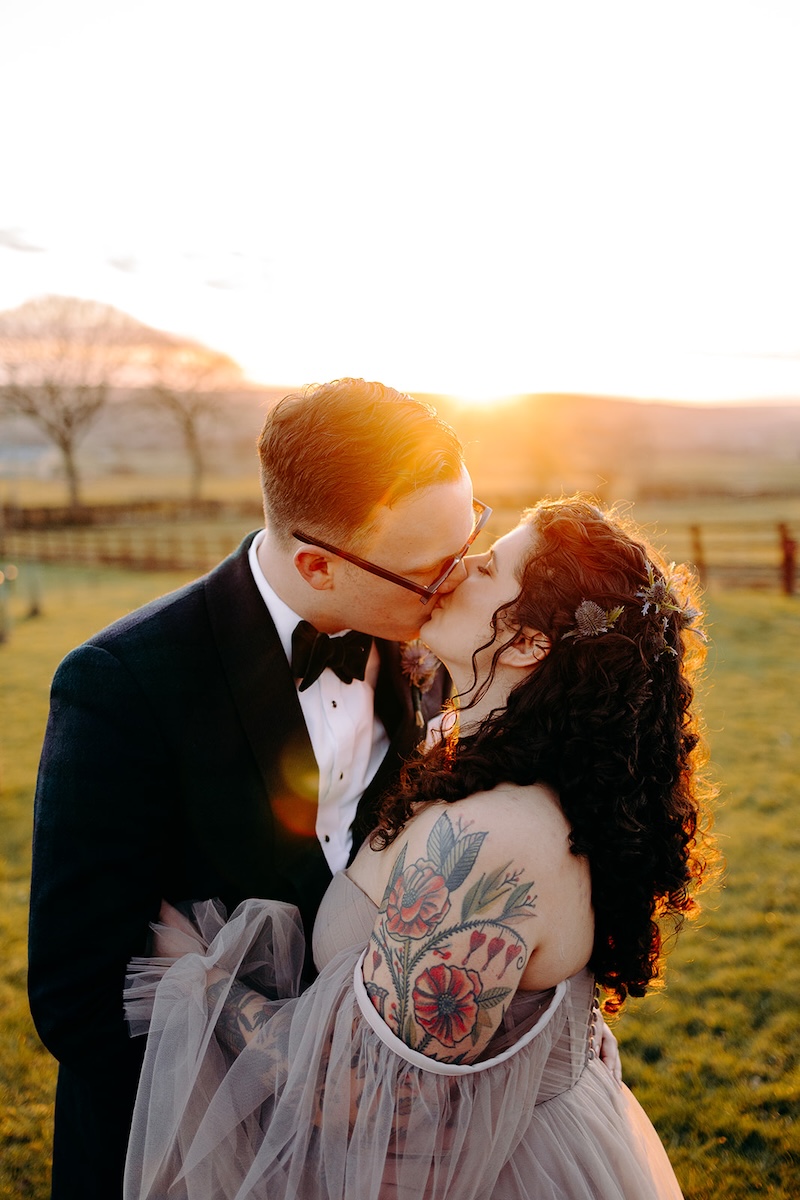 Bride and groom standing together overlooking the countryside at The Wellbeing Farm during sunset wedding photography.