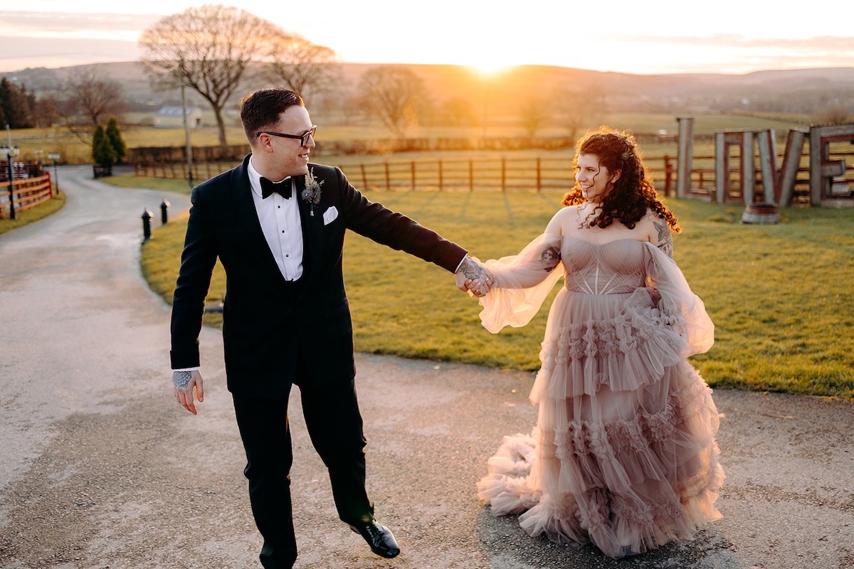 Bride and groom walking across the fields at sunset during golden hour portraits at The Wellbeing Farm, photographed by a wedding photographer.