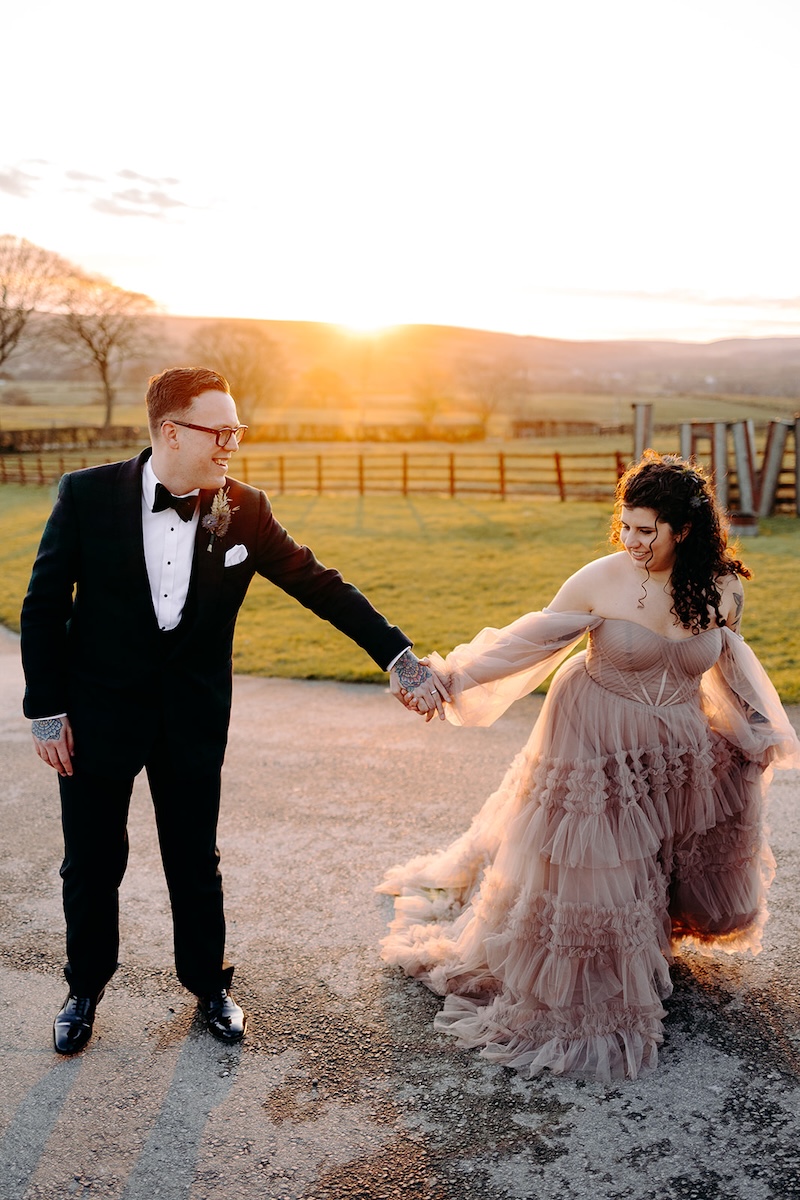 Bride and groom walking across the fields at sunset during golden hour portraits at The Wellbeing Farm, photographed by a wedding photographer.